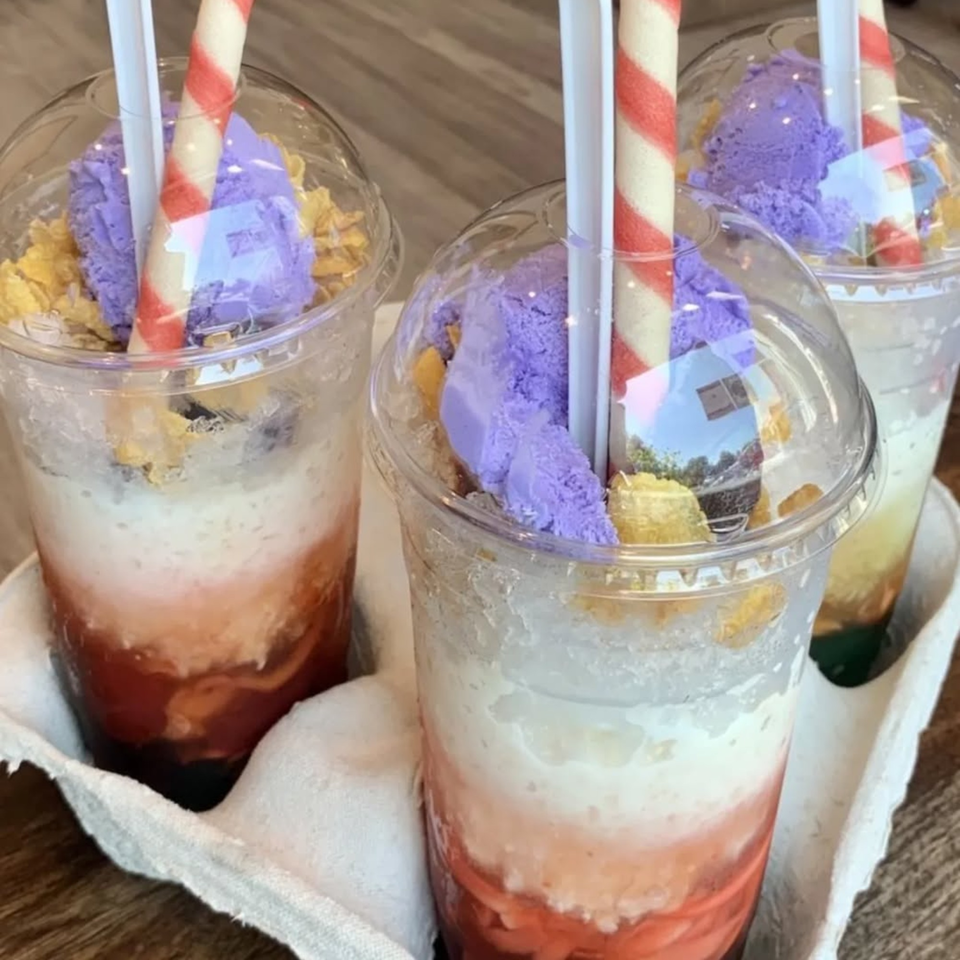 Three Filipino Halo-Halo desserts in clear cups with purple ube ice cream and striped straws.