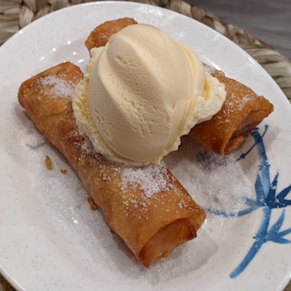 Two golden-brown Filipino turon, sprinkled with sugar, topped with a scoop of vanilla ice cream.