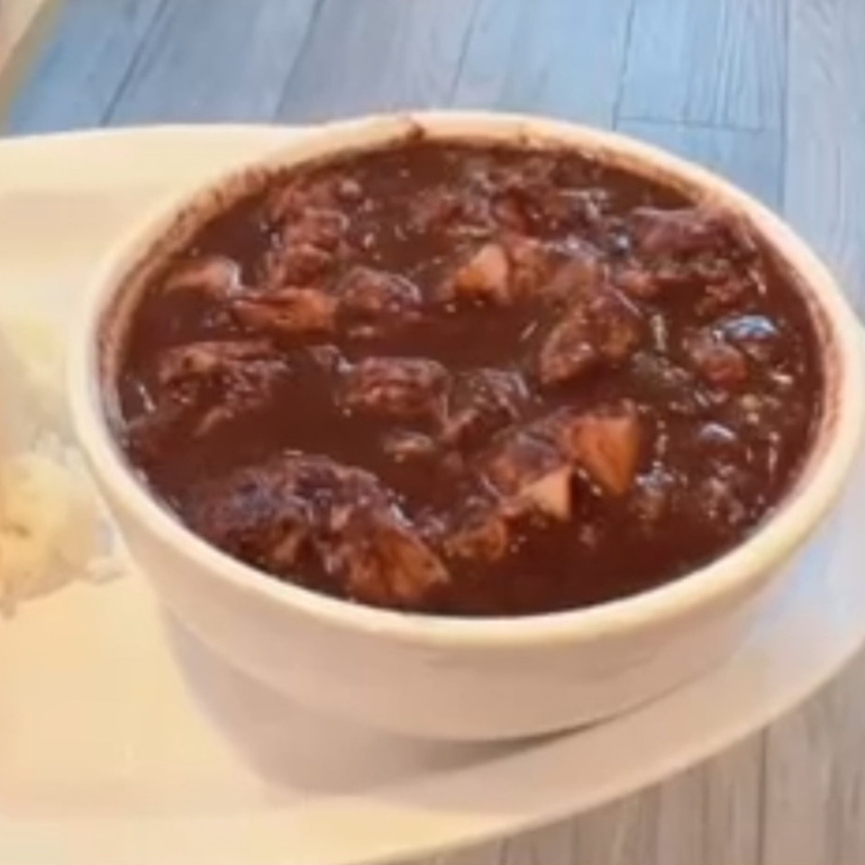 A white bowl of Kuya’s Islander Cuisine's Filipino dinuguan, a dark stew with meat pieces, next to rice.