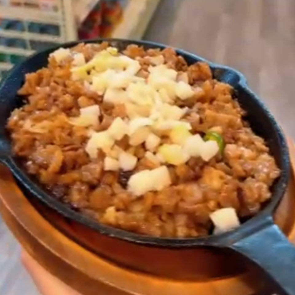 Sizzling Filipino sisig, a savory chopped meat dish, topped with diced onions in a cast iron skillet.