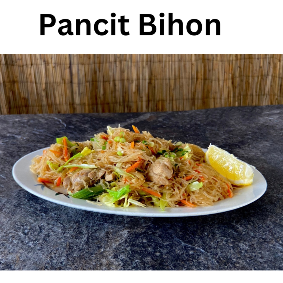 Filipino Pancit Bihon noodles with chicken, vegetables, and a lemon wedge on a white plate.