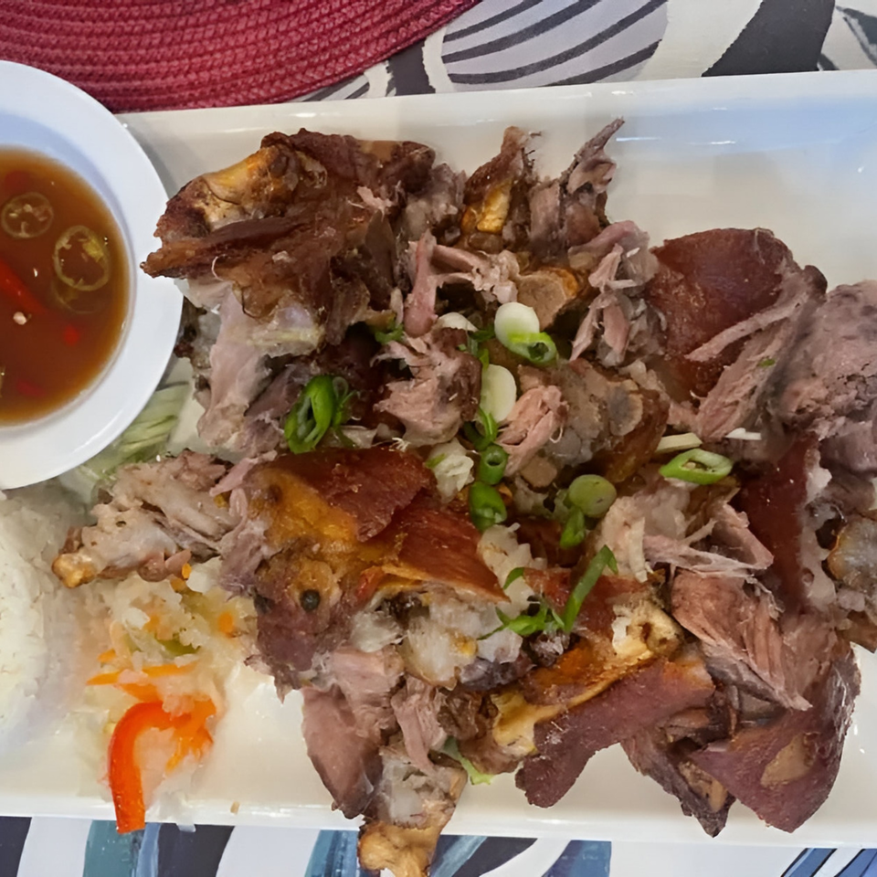 Crispy pata, a Filipino deep-fried pork hock dish, with dipping sauce and pickled vegetables.