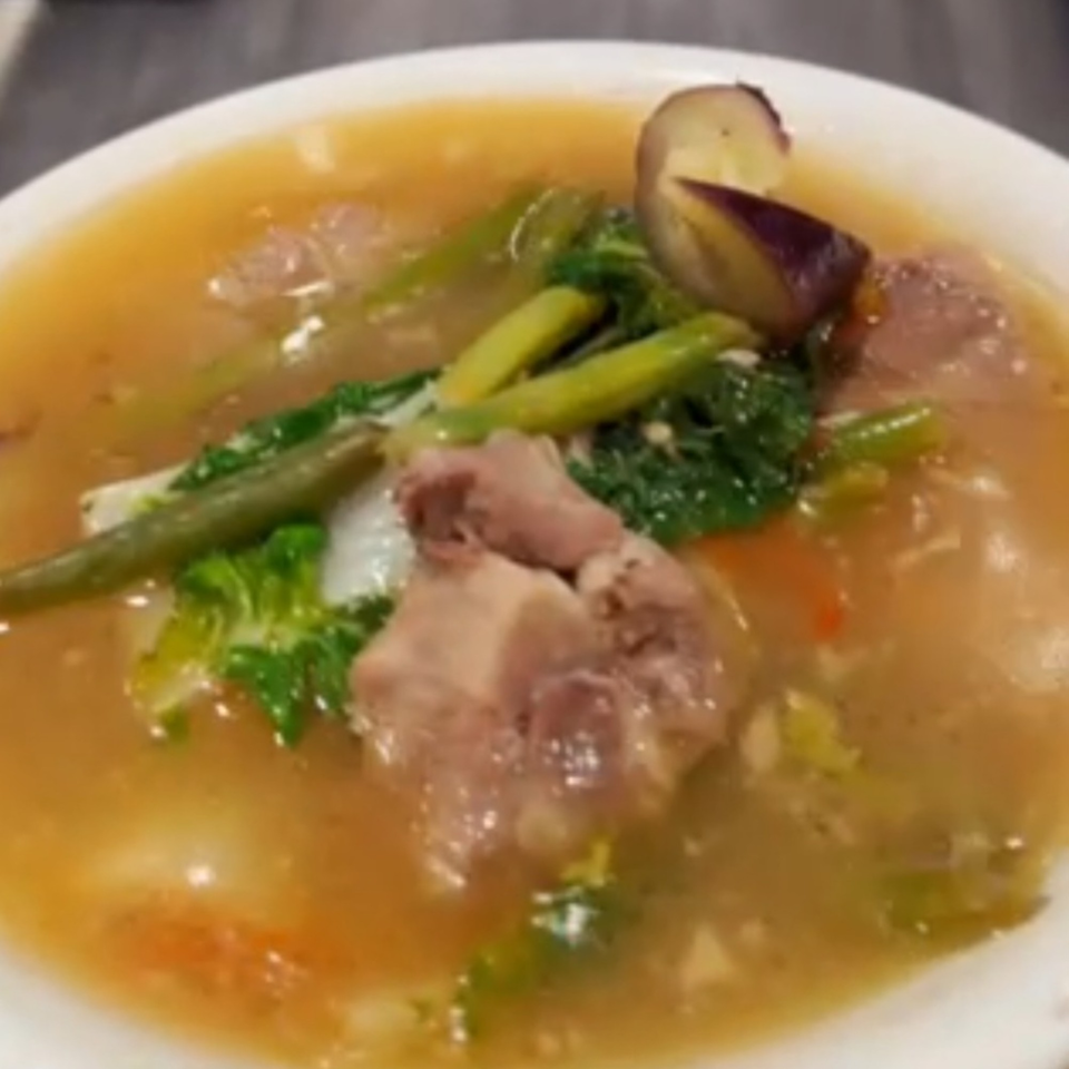 A bowl of Kuya’s Islander Cuisine's Filipino Sinigang with meat, green beans, and eggplant.