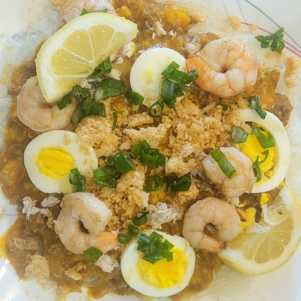 Filipino Pancit Palabok with shrimp, sliced eggs, lemon, and green onions on a white plate.