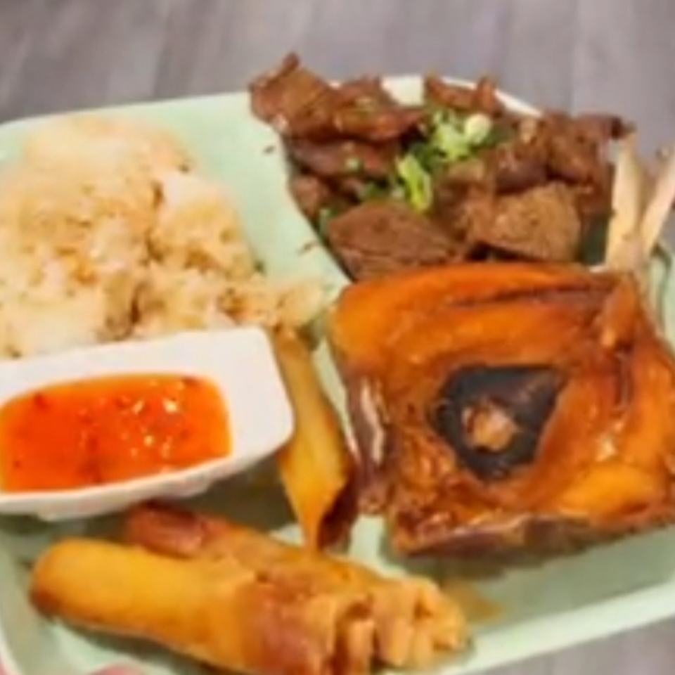 A Filipino meal with fried fish, meat, rice, lumpia, and sweet chili sauce on a green plate.