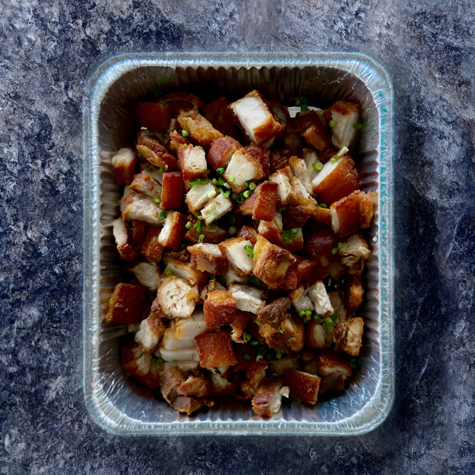 Crispy Filipino Lechon Kawali, deep-fried pork belly pieces, in a foil takeout container.