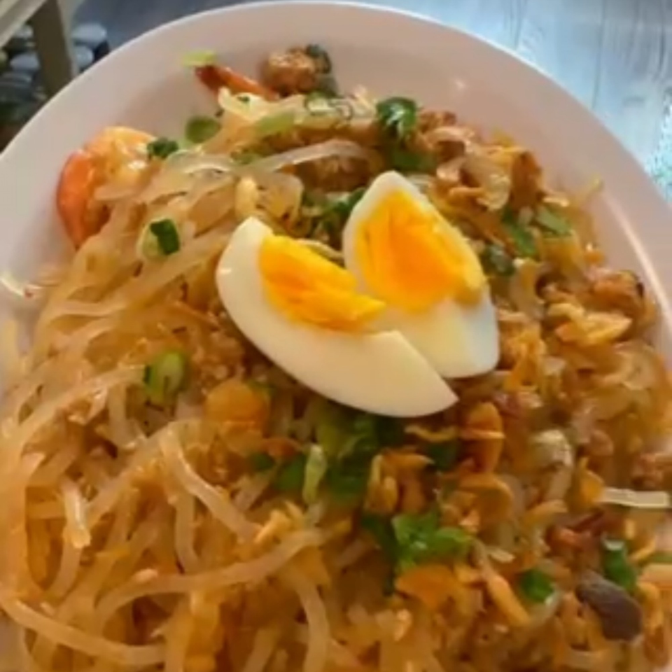 Filipino Pancit Palabok with shrimp, crushed chicharon, and sliced hard-boiled eggs on a white plate.